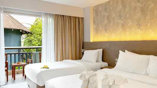 To opdækkede enkeltsenge med dekorative håndklæder og blomster. Udsigt over en møbleret altan med grønne områder og bygning. (AI-genereret tekst)