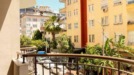 Udsigt fra en altan mod en gade omgivet af bygninger og grønne områder. (AI-genereret tekst)