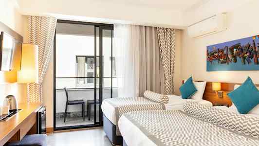 Et hotelværelse med to enkeltsenge, en altan med møbler og et skrivebord med lampe og elkedel. (AI-genereret tekst)