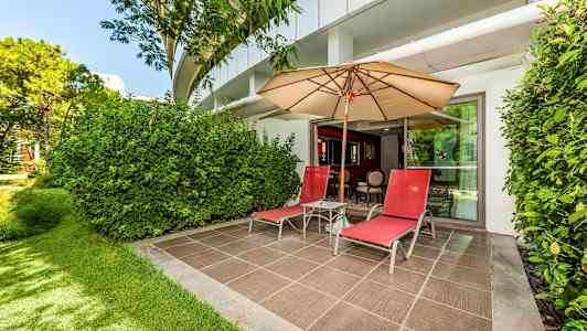 En terrasse med to røde liggestole, en parasol og grønne omgivelser. (AI-genereret tekst)