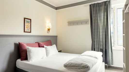 Billede af et hotelværelse med en dobbeltseng, dekoreret med sengetøj i hvidt og rødt samt en lys grå sengegavl. (AI-genereret tekst)