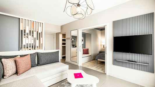 Et rummeligt og moderne indrettet hotelværelse med siddeområde, soveplads og en vægmonteret TV. (AI-genereret tekst)