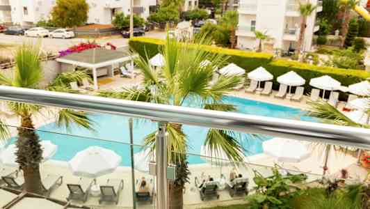 Udsigt fra altanen med en pool, parasoller og liggestole omgivet af planter. (AI-genereret tekst)