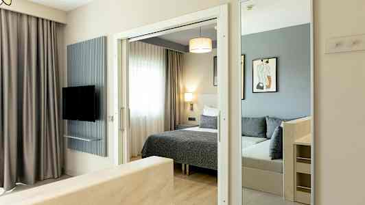 Billede af et hotelværelse med seng, spejl og tv. (AI-genereret tekst)