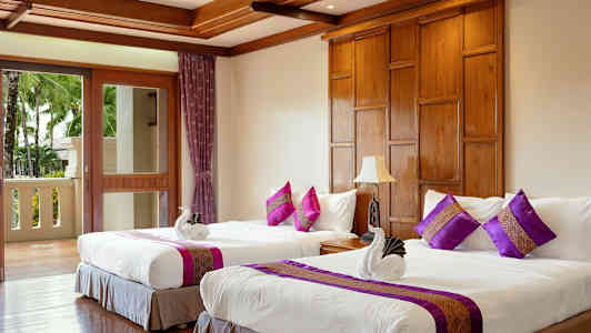 Et hotelværelse med to enkeltsenge dekoreret med lilla puder og håndklæder formet som svaner. (AI-genereret tekst)