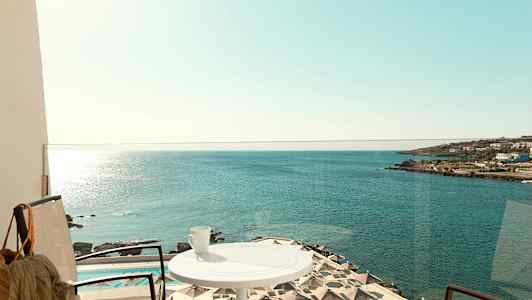 En balkon med udsigt over havet, parasoller ved en pool og en kop på et bord. (AI-genereret tekst)