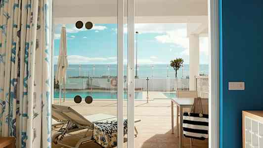 Billede af en liggestol og en pool set fra en terrasse gennem glasdøre. (AI-genereret tekst)