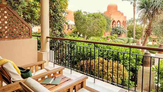 En terrasse med træstole og udsigt over en frodig have og bygninger med bueformede vinduer. (AI-genereret tekst)