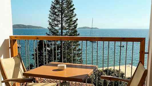 En balkon med to stole og et bord, havet og en mast er synlige i baggrunden. (AI-genereret tekst)