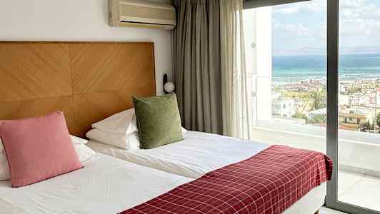 Et hotelværelse med to enkeltsenge, en stor glasdør med udsigt til havet og faciliteter som aircondition. (AI-genereret tekst)