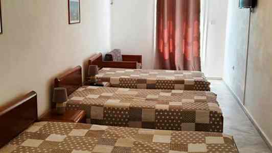 Tre enkeltsenge på et hotelværelse med brunmønstrede sengetæpper, aircondition og et TV på væggen. (AI-genereret tekst)