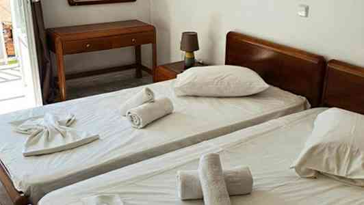 To enkeltsenge med hvide lagener og håndklæder placeret ovenpå, samt et bord og et spejl i rummet. (AI-genereret tekst)