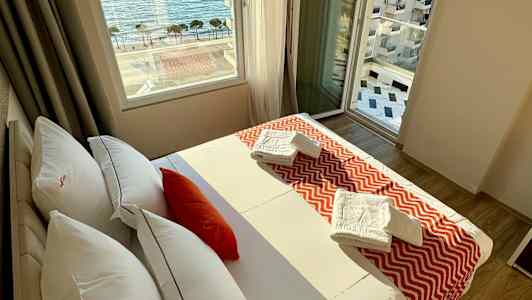 Et hotelværelse med en seng, vindue med havudsigt og håndklæder på sengen. (AI-genereret tekst)