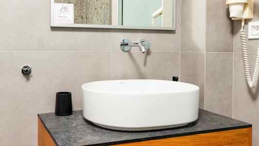 Et badeværelse med en rund vaskeskål på et træskab, et spejl ovenover og detaljer som en bruser og hårtørrer synlige. (AI-genereret tekst)