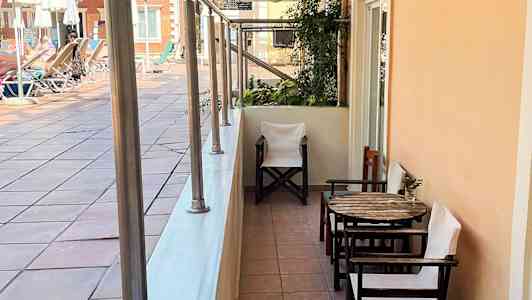 En terrasse med bord og stole ved en gangsti tæt på et poolområde. (AI-genereret tekst)