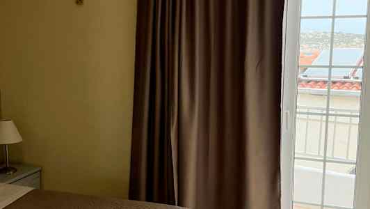 To senge med brune sengetæpper, et vindue med gardiner og udsigt til bygninger udenfor. (AI-genereret tekst)