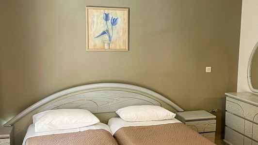 To enkeltsenge med brune sengetæpper, et maleri på væggen ovenover og en kommode til højre. (AI-genereret tekst)