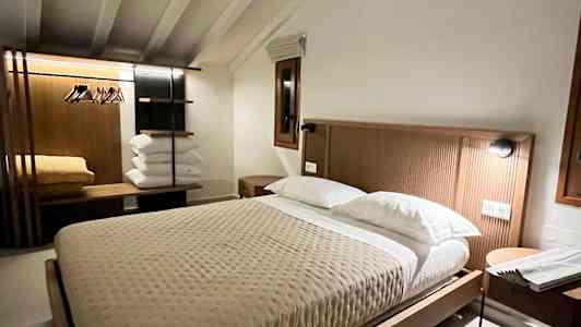 Et varmt indrettet soveværelse med en stor seng, natbord og et klædestativ. (AI-genereret tekst)