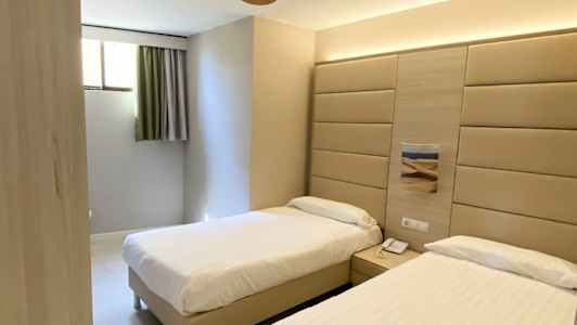 Et hotelværelse med to enkeltsenge, vægpanel bag sengene og en loftsventilator. (AI-genereret tekst)