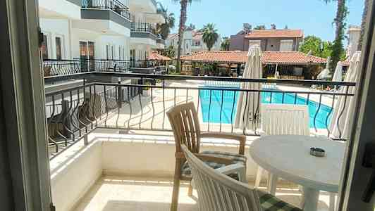 Udsigt fra en altan over et poolområde og tilstødende bygninger. (AI-genereret tekst)