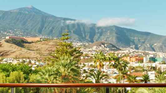 En altan med bord, hvor mad og drikke er serveret, udsigt over en by med bjerge i baggrunden. (AI-genereret tekst)