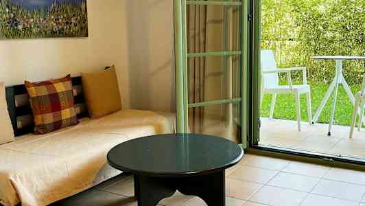 Værelse med sofaer, et bord og en åben dør til en frodig terrasse. (AI-genereret tekst)