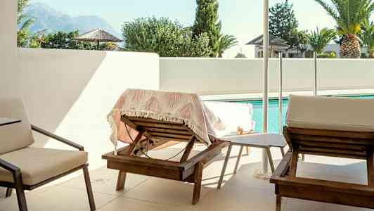 Billede af en terrasse med liggestole, parasol og swimmingpool i baggrunden. (AI-genereret tekst)