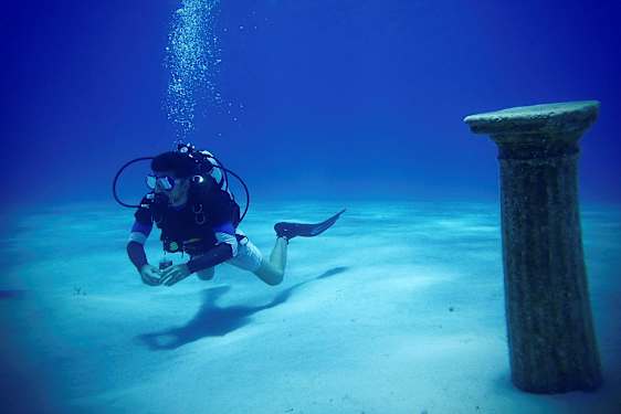 En dykker under vandet tæt på en antik søjle på havbunden. (AI-genereret tekst)