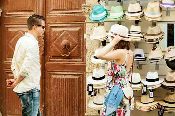 En person prøver en hat ved et salgsbord med forskellige hatte. (AI-genereret tekst)