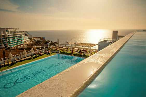 Udendørs swimmingpool med liggestole og udsigt over havet ved solnedgang. (AI-genereret tekst)