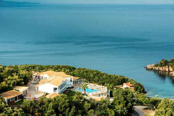 Hotelbygning med pool og omkringliggende grønt områder ved havet. (AI-genereret tekst)