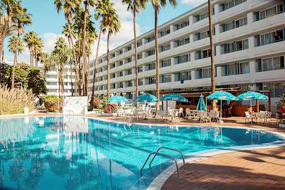 Udendørs pool med liggestole og parasoller foran et stort hotel. (AI-genereret tekst)