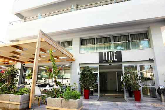 Hotelindgang med skilt, der viser 'Elite Hotel', omgivet af planter og blomster. (AI-genereret tekst)
