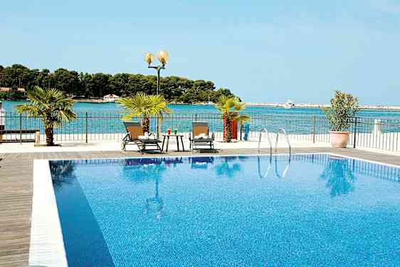 En pool med klart blåt vand og to liggestole ved siden af. Havet er synligt i baggrunden. (AI-genereret tekst)