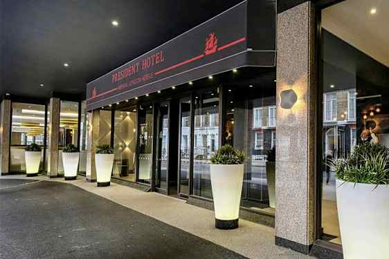 Indgangen til President Hotel med store hvide krukker fyldt med grønt. (AI-genereret tekst)