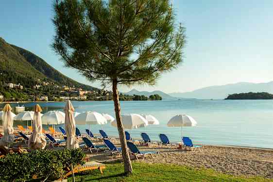 En strand med liggestole, parasoller og udsigt over havet med bjerge i baggrunden. (AI-genereret tekst)