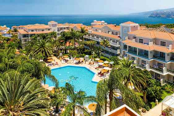 Hotel med poolområde og omkringliggende grønne områder ved kysten. (AI-genereret tekst)