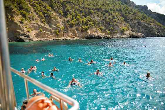 Badesende personer i klart blåt vand foran en klippekyst. (AI-genereret tekst)