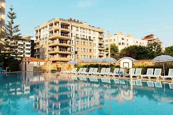 Billede af en pool med solsenge og parasoller ved siden af, samt en bygning i baggrunden. (AI-genereret tekst)