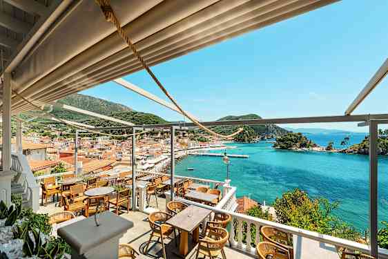 Udsigt fra restaurant til en bugt med bådpladser, farverige huse og grønne bakker. (AI-genereret tekst)