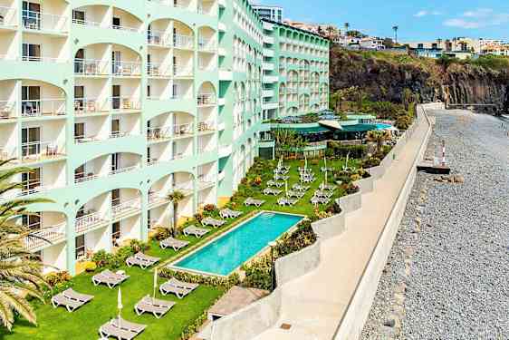 Et hotel med flere etager ved havet, græsplæne med liggestole og pool udenfor. (AI-genereret tekst)