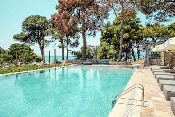 Udendørs swimmingpool omgivet af liggestole, grønne områder og havudsigt. (AI-genereret tekst)