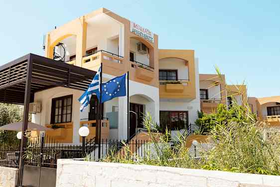 En bygning med gul og hvid facade samt flag der viser Grækenland og EU. (AI-genereret tekst)