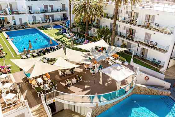 Et billede af et hotelresort med en stor pool omgivet af liggestole og parasoller. I forgrunden er en udendørs bar med mange siddepladser under skyggende sejl. (AI-genereret tekst)