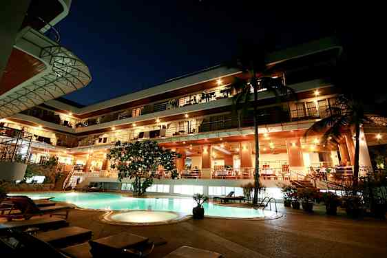 Aftenudsigt af en fleretagers bygning med oplyst facade og en pool i forgrunden. (AI-genereret tekst)