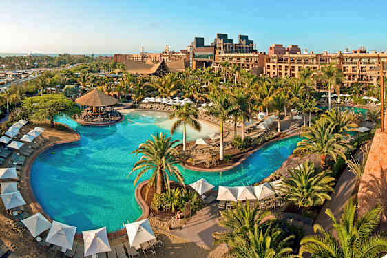 En stor udendørs pool omgivet af parasoller, liggestole og grønne omgivelser ved et ferieresort. (AI-genereret tekst)