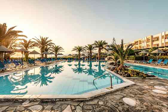 Udendørs pool med liggestole og parasoller ved solnedgang. (AI-genereret tekst)