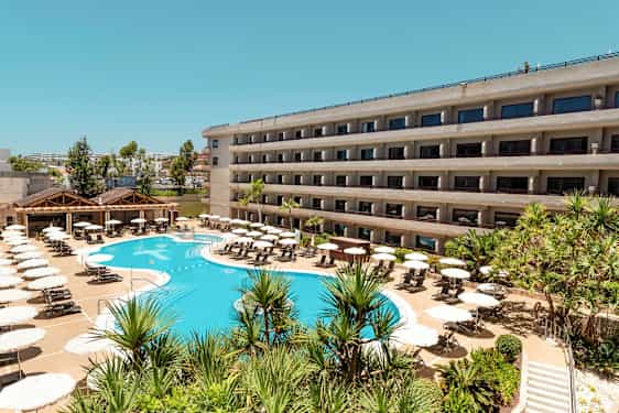 En hotelbygning med altaner og en pool omgivet af solsenge og parasoller. (AI-genereret tekst)