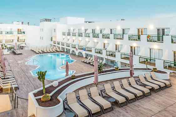 En hotelpool med liggestole og en hvid bygning omkring. (AI-genereret tekst)