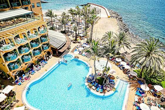 En hotelpool ved kysten med palmer og liggestole omkring. (AI-genereret tekst)